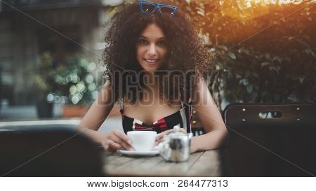 Cheerful Cute Girl In Sunglasses Is Sitting At The Table Of A Street Cafe With A Cup Of Tea; Young M