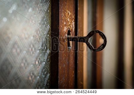 Close-up Shot Of An Old Rusty Key Inside A Keyhole Of An Old Cherry Wood Kitchen Cupboard