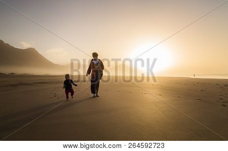 Silhouette of young mother with her little child walking on sunshine in Cofete, Fuerteventura, Canary Islands, Spain.