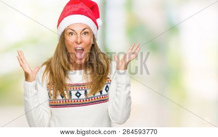 Middle age adult woman wearing winter sweater and chrismat hat over isolated background celebrating crazy and amazed for success with arms raised and open eyes screaming excited. Winner concept