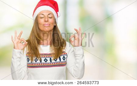 Middle age adult woman wearing winter sweater and chrismat hat over isolated background relax and smiling with eyes closed doing meditation gesture with fingers. Yoga concept.