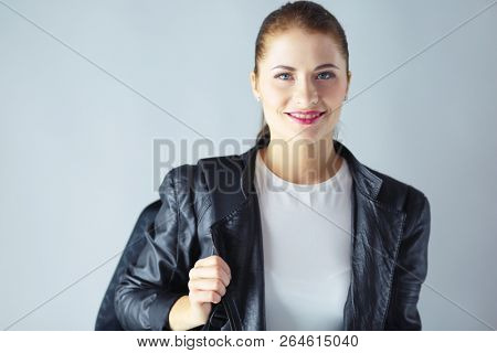 portrait of beautiful young brunette woman in stylish black jacket on gray.