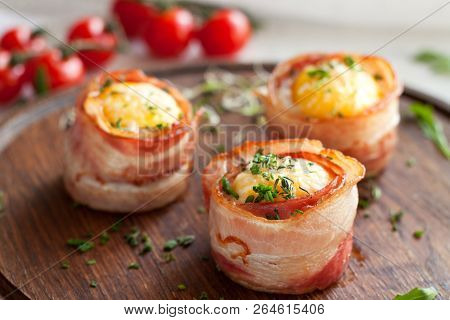 Tasty Egg Muffins Wrapped In Crispy Bacon On Round Wooden Serving Board Garnished With Greens And Ch