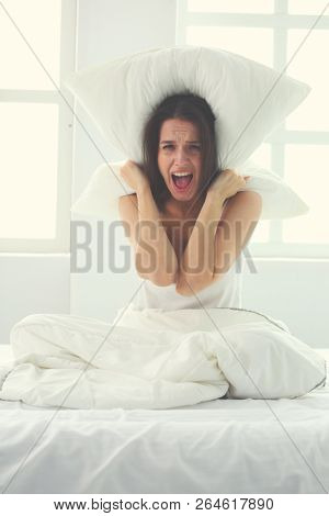 Young caucasian woman covering her head and ears with pillows.