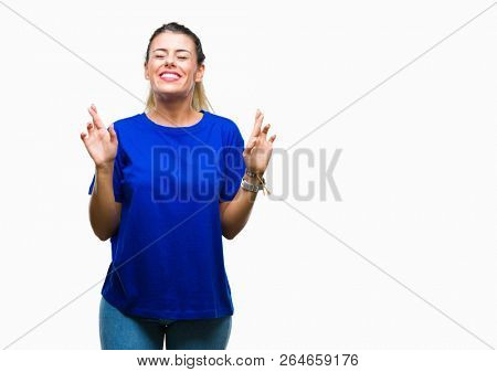 Young beautiful woman wearing casual blue t-shirt over isolated background smiling crossing fingers with hope and eyes closed. Luck and superstitious concept.
