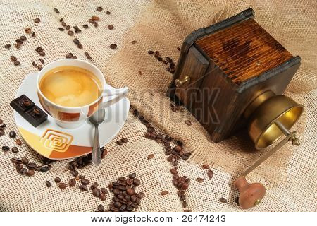 Kaffeetasse umgeben von Kaffee Körner und Kaffeemühle im Hintergrund