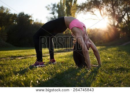 Girl Is Doing Yoga, Standing In Bridge Pose. Setu Bandhasana. With Sunset On Background.in A Park In