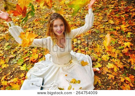 Autumn fashion feminity lace dress with long sleeve in princess style. Top view of girl model trew foliage bouquet sitting on fall leaves in city park outdoor.