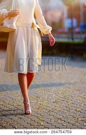 Fashion woman in autumn-spring dress on city street. Cropped shot of female style of feminine fashionable girl model wallking hight heel fall outdoor. Color tone on shiny sunlight background.