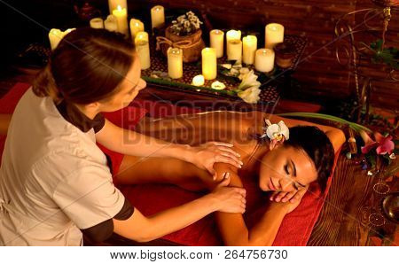 Deep tissue massage treatment in Ayurveda of woman in spa salon. Girl on candles background treats problem back. Luxary Filipino therapy interior with working masseuse.