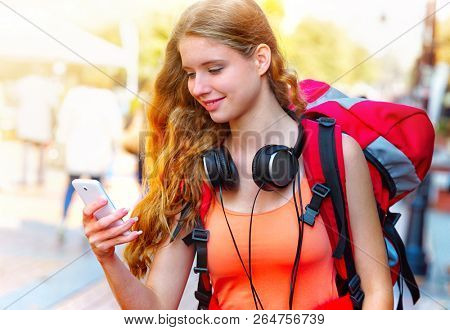 Smartphone with GPS navigator in hands of tourist girl with backpack and headphones looking for way by smartphone at cultural city pedestrianized street outdoor.