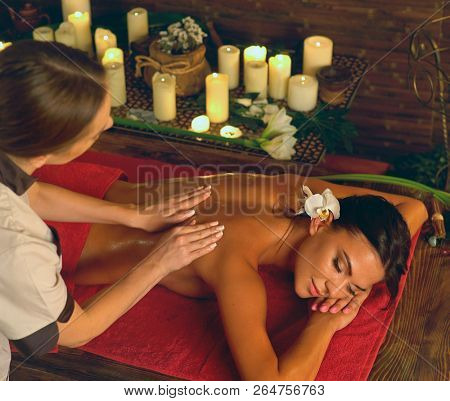 Deep tissue massage treatment in Ayurveda of woman in spa salon. Top view girl on candles background treats problem back. Luxary Filipino therapy interior with working masseuse.