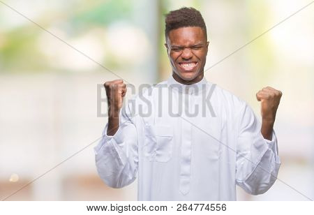 Young arabic african man wearing traditional djellaba over isolated background celebrating surprised and amazed for success with arms raised and open eyes. Winner concept.