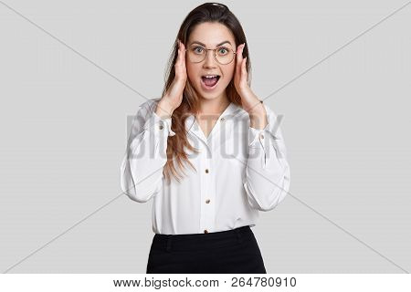 Photo Of Astonished Woman Keeps Both Hands On Head, Opens Mouth Widely, Reacts On Sudden News In Off