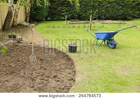 Preparing A Freshly Dug Flower Bed For Planting In A Garden With Fork And Wheelbarrow
