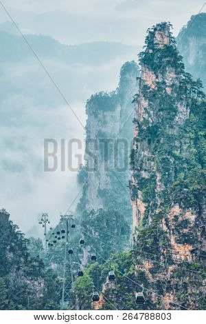 Famous tourist attraction of China - Zhangjiajie stone pillars cliff mountains in fog clouds with cable railway car lift at Wulingyuan, Hunan, China. With camera pan