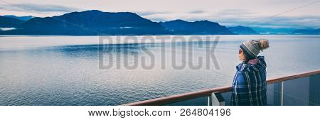Alaska cruise travel luxury vacation woman banner panorama of inside passage scenic landscape background on balcony deck enjoying view of mountain range. Asian girl tourist with wool blanket.