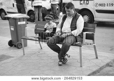 Barcelona, Spain - March 30, 2016: Father Man And Little Girl Search In Smartphones Sitting On Bench
