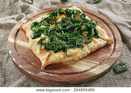 Homemade Square Khachapuri Made From a Delicious Tender Dough with Spinach, Melted Cheese and Butter Close Up. Traditional Hachapuri Topped with Spinacia Leaves on Wooden Rustic Background