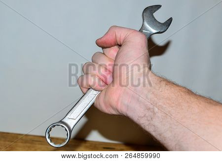 Large Metal Wrench In Man's Hand On White Wall Background. Construction Tool. Plumber