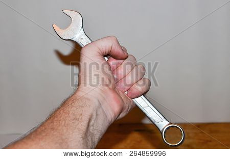 Large Metal Wrench In Man's Hand On White Wall Background. Construction Tool. Plumber