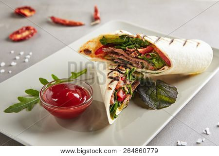 Barbeque Meat Shaverma or Doner Kebab with Vegetables on White Plate. Thin Tortilla Rolls Stuffed with Sliced Fried Beef, Pork and Chicken Fillet Cucumber, Tomato, Sauce, Paprika and Greens