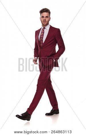 relaxed elegant man walks on white background with a hand in pocket and looks up to side, full body picture