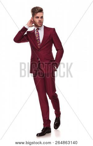 relaxed elegant man walks on white background with a hand in pocket and looks to side while holding neck