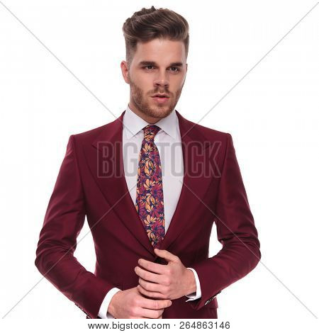 portrait of elegant young man in grena suit looking down to side while holding palms together