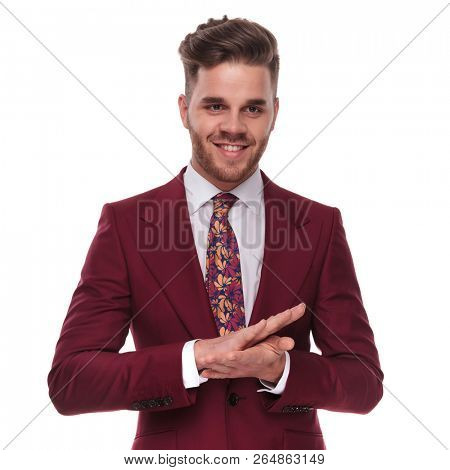 portrait of happy businessman wearing a grena colored suit rubbing his palms together and looking down to side while standing on white background