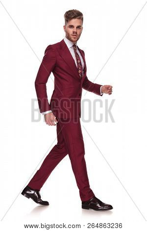 side view of young businessman with parted lips walking on white background while wearing a grena suit