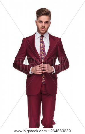 portrait of seductive young man buttoning his grena colored suit while standing on white background