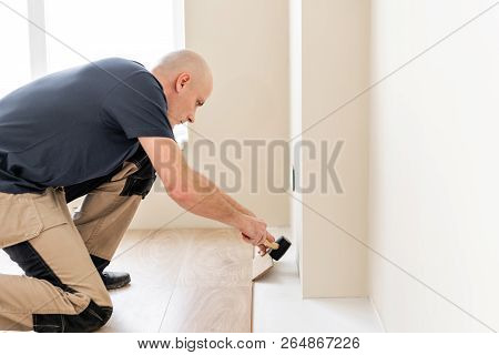 Male Worker Installing New Wooden Laminate Flooring On A Warm Film Foil Floor. Infrared Floor Heatin