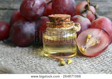 Bottle Of Organic Grape Seed Oil For Spa And Bodycare And Fresh Ripe Grapes Berries On Old Wooden Ta