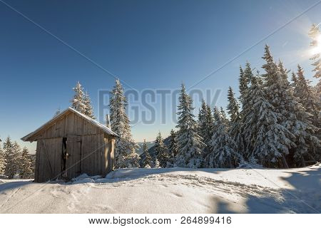 Fairy Tale Beautiful Winter Sunny Landscape. Wooden Shepherd Hut On Mountain Snowy Clearing Among Ta