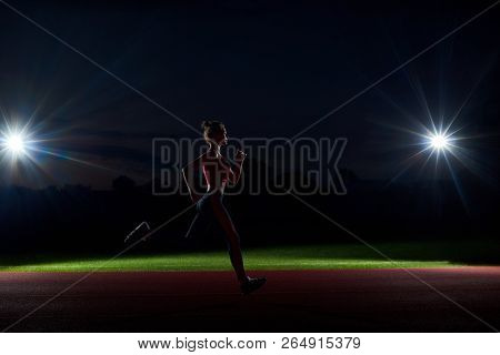 Side View Of Silhouette Of Woman Running Forward In Darkness On Stadium Only With Two Lights From Tw