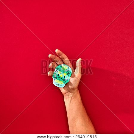 Paper handmade craft skull Calaveras attributes of the Mexican holiday Calaca holds the hand of a man on a red background with space of text. Holiday Halloween