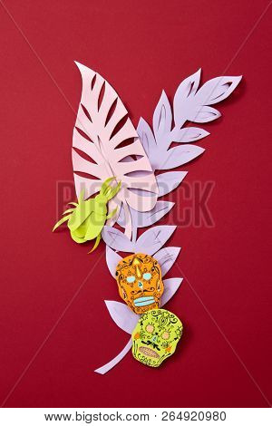 Calaveras attribute of the Mexican holiday of Calaca and handcraft paper colored leaves on a red background with copy space for text. Creative Halloween postcard.
