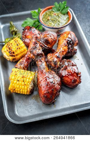 Traditional barbecue chicken drumsticks with corn and chimichurri sauce as top view in a silber fryer 