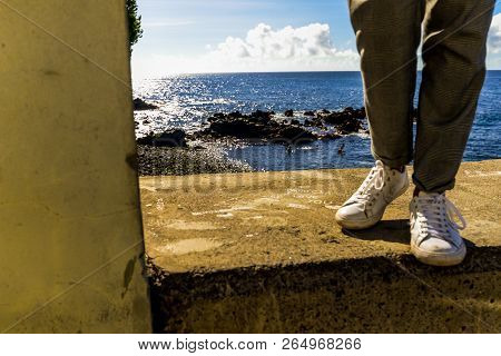 A Woman On A Ledge Next To The Ocean In Funchal - Maderia, Portugal