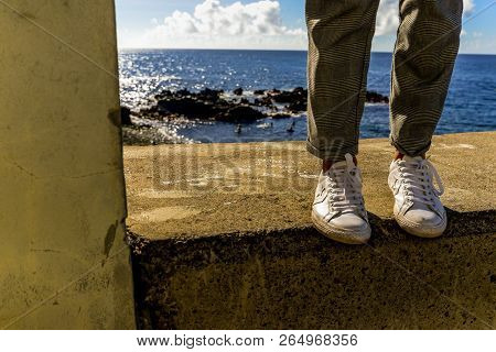 A Woman On A Ledge Next To The Ocean In Funchal - Maderia, Portugal