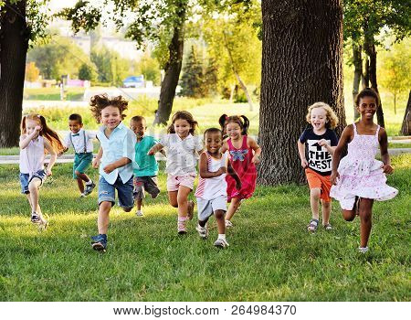 A Group Of Preschoolers Running On The Grass In The Park.
