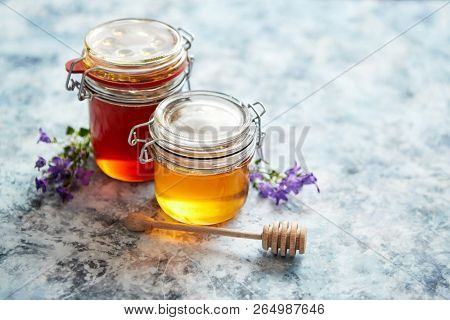 Jars with different kinds of fresh organic honey placed in a row on a blue stone background