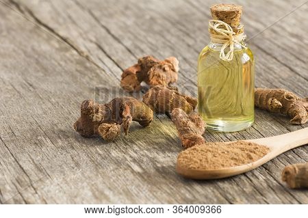 Glass Bottle Of Galangal Essential Oil, Root And Galanga Powder In Wooden Spoon On Rustic Table. Hea