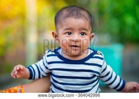 A Baby Boy Looking And Smiling. Dressed Are White And Navy Blue Striped Dress. Baby Candid Shoot. Ba