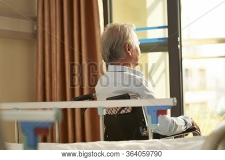 Rear View Of Senior Asian Man Sitting In Wheel Chair In Nusing Home Or Hospital Ward Looking Out Of 