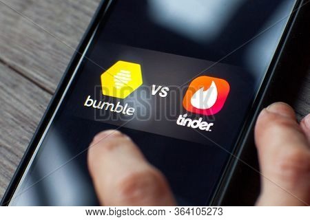 Young Woman Holding A Smartphone With A Bumble Vs Tinder Dating Icons On Screen. Iphone 11 With A So