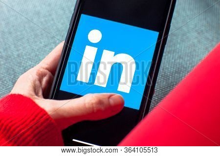 Young woman holding a smartphone with Linked in app on screen. IPhone 11 with a social media profess