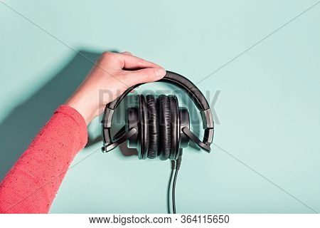 Woman Holding Black Overhead Headphones On Blue Background, Copy Space. Modern Technology Flat Lay W