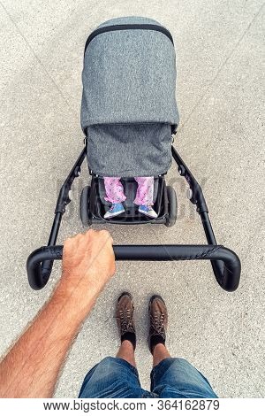 Legs Of Infant Girl Lying In Baby Stroller. Hand Of Father Pushing  A Pram